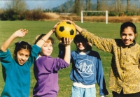 Four girls on a soccer field touching yellow soccerball