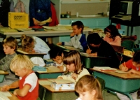 Young children at desks doing schoolwork, some have boxes on their desks C.1987/88