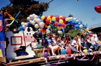 People siting on parade float wtih balloons and cow statue (Pitt Meadows Day 2004?). Balloons on far right have 