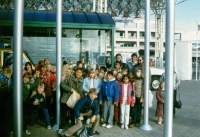 Group of children and supervisors smiling for camera outside around flagpoles C. 1986/87