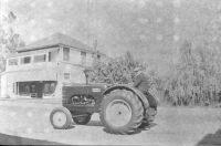 Hans on tractor in front of General Store, with upper porch. 1950s